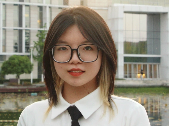 Jialij Li stands wearing a shirt and tie in front of a lake and building with lots of glass doors and windows in the background