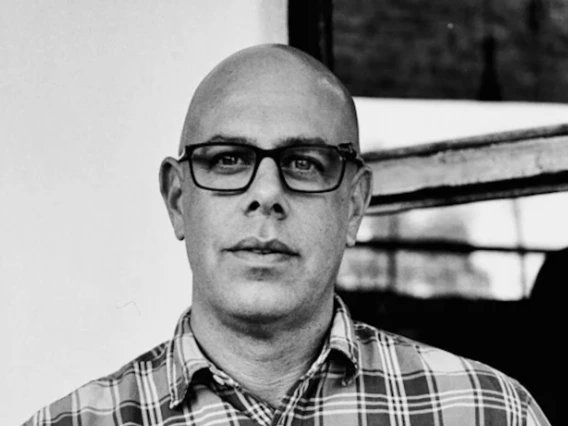 Photo of Dr. Stefano Bloch in black and white, wearing black framed glasses and a checkered shirt