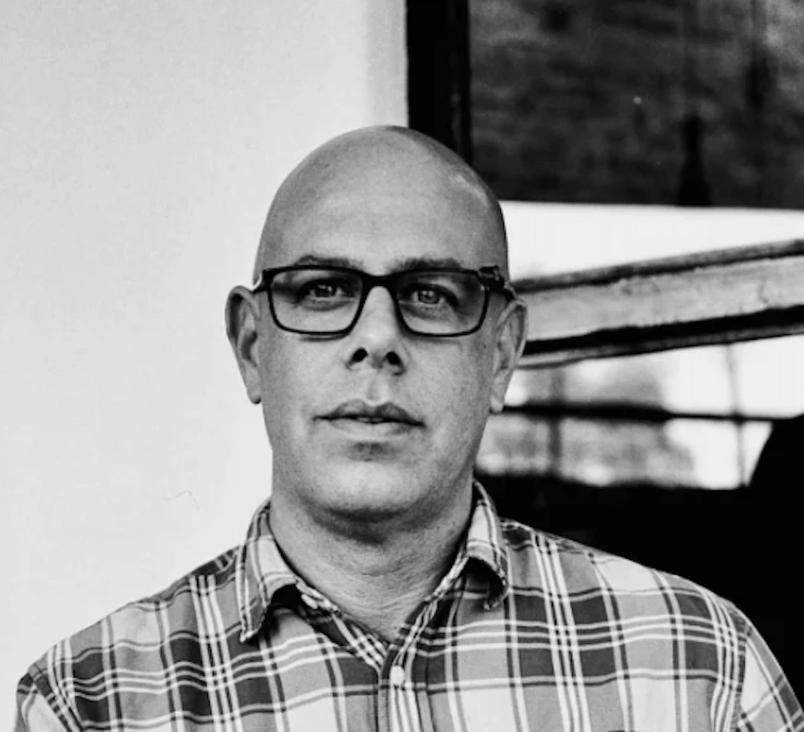 Photo of Dr. Stefano Bloch in black and white, wearing black framed glasses and a checkered shirt