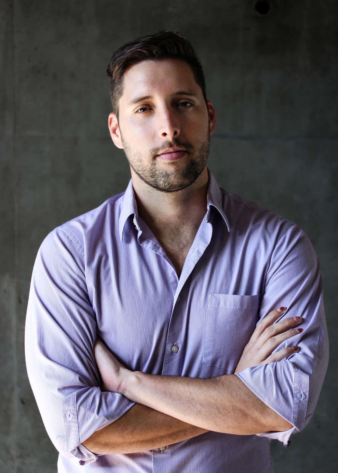 Professional photo of Lucas Belury standing in front of a matte background wearing a collared buttondown shirt with his arms crossed