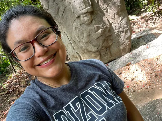 Xanti Ceballos Pesina stands in front of a carven piece of Mayan architecture with forest in the background