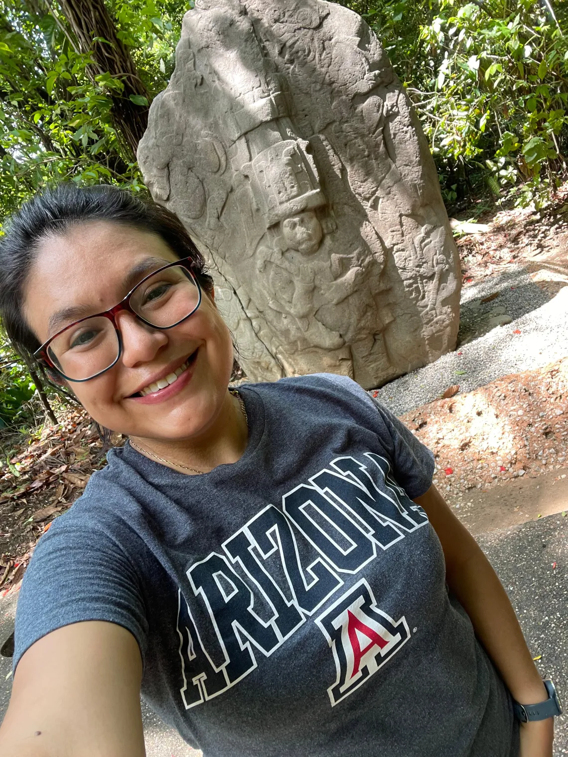 Xanti Ceballos Pesina stands in front of a carven piece of Mayan architecture with forest in the background